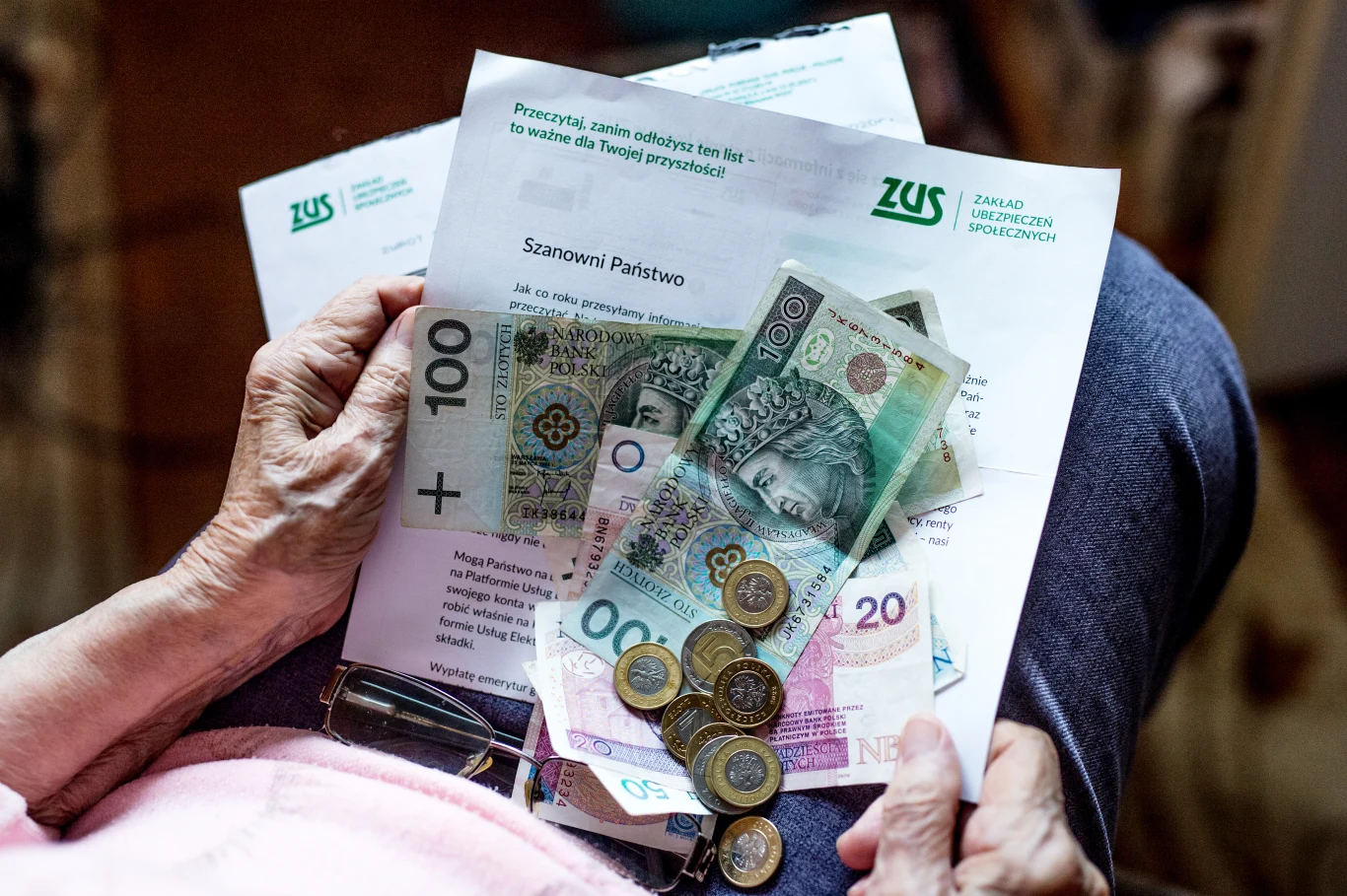Urzędy skarbowe wzywają seniorów do zwrotu ulgi w PIT. Głównym powodem jest pobieranie renty rodzinnej Koperta i dokumenty z logo ZUS, polskie banknoty i monety na kolanach starszej osoby, obok okulary do czytania