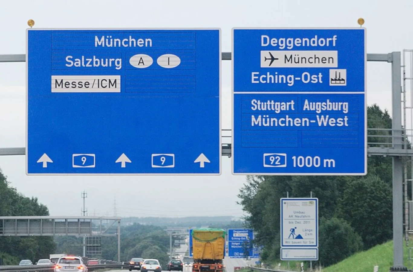 Biała kreska na znaku drogowym z miejscowościami - co oznacza? Biała kreska na niebieskiej tablicy drogowej z nazwami miejscowości i numerami tras nad autostradą w Niemczech.