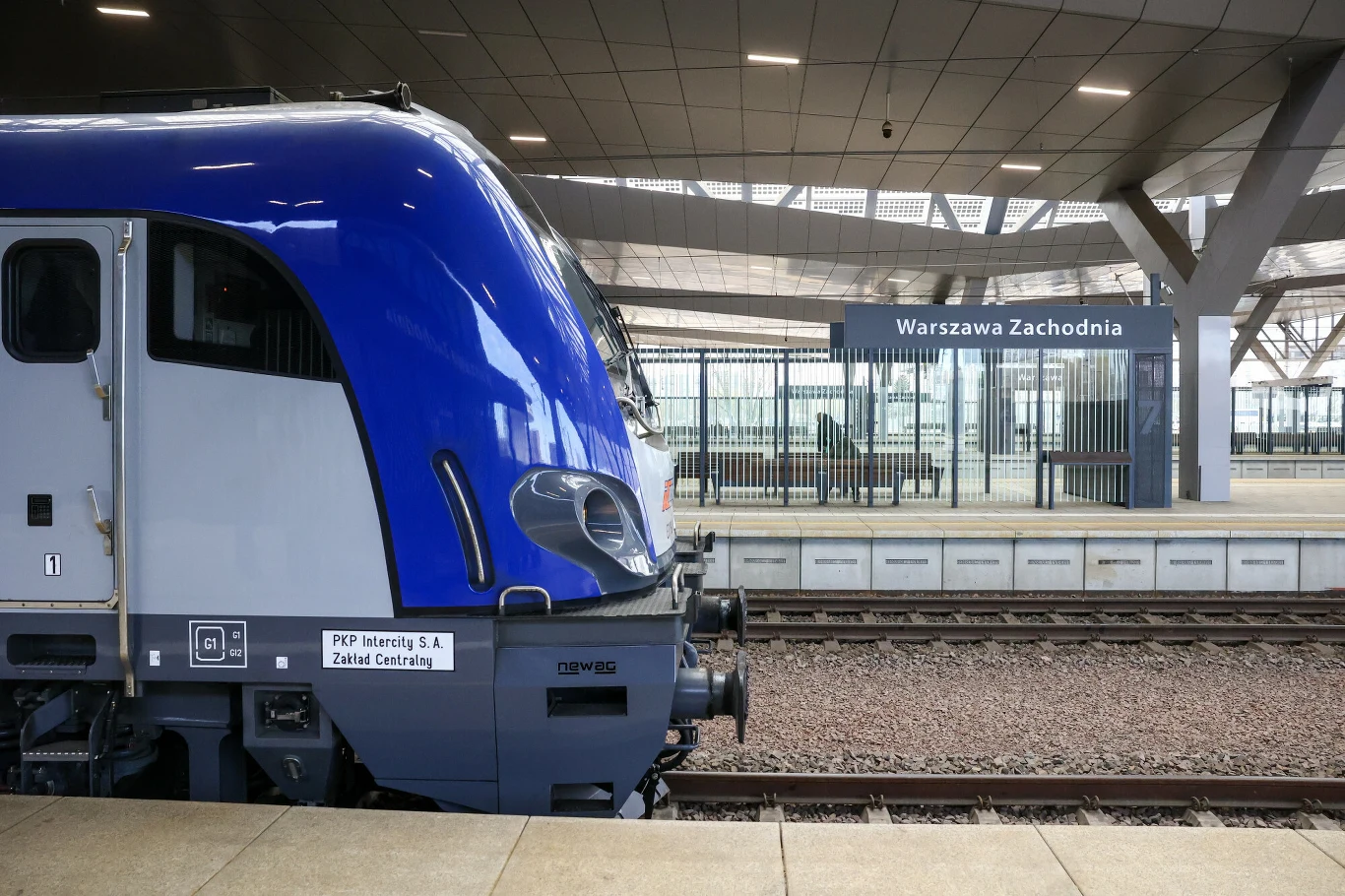 nowoczesna, niebieska lokomotywa elektryczna stoi przy peronie na stacji kolejowej Warszawa Zachodnia, w tle widoczny peron zadaszony oraz tablica z nazwą stacji
