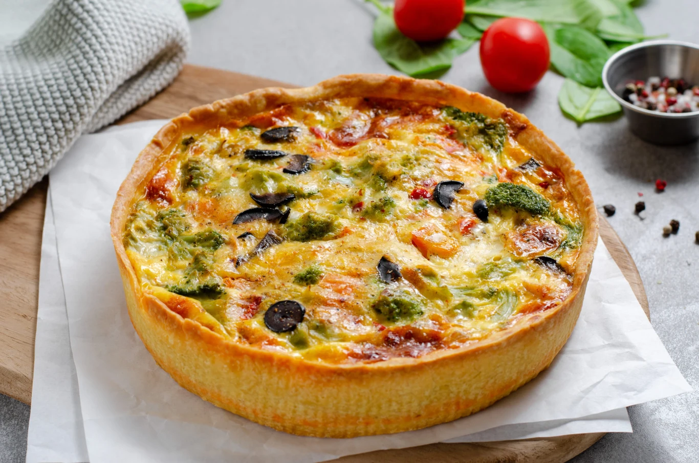 Quiche with Vegetables, Homemade Open Pie, Savory Tart on Bright Background Wytrawna tarta z warzywami, serem, oliwkami i pomidorami, podana na jasnym tle.