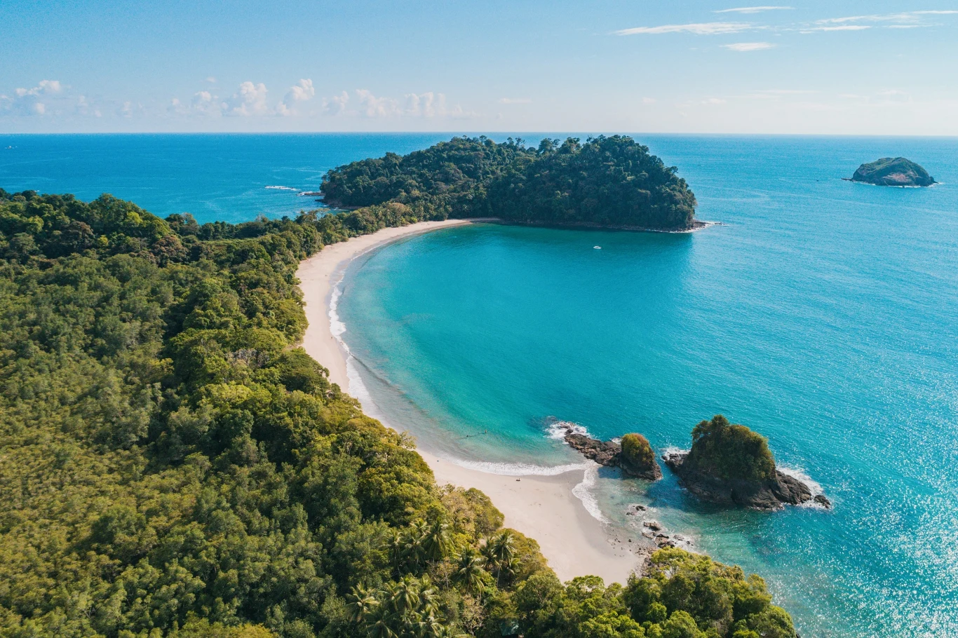 Kostaryka będzie spełnieniem marzeń dla pań kochających rajskie plaże i bujną roślinność Piaszczysta, półokrągła plaża otoczona gęstą tropikalną roślinnością, turkusowe morze z delikatnymi falami oraz dwie niewielkie skaliste wyspy w oddali.