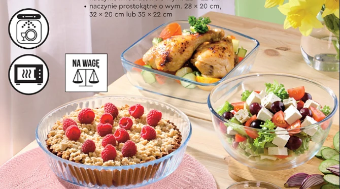 okrągłe naczynie z kruchym ciastem posypanym malinami, prostokątne naczynie z pieczonymi udami kurczaka na warzywach oraz szklana miska z sałatką grecką z kostkami sera feta, oliwkami i warzywami ustawione na drewnianym stole obok żółtych kwiatów