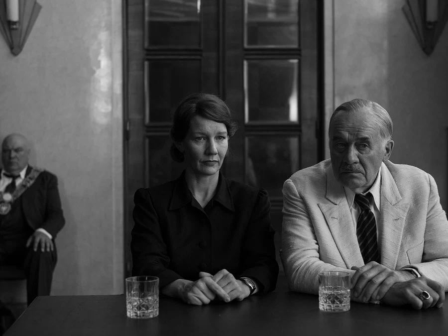 Sandra Hüller i Hanns Zischler w scenie z filmu "Fatherland" Sandra Hüller i Hanns Zischler przy stole w scenie z filmu "Fatherland", czarno-białe ujęcie, w tle urzędnik.