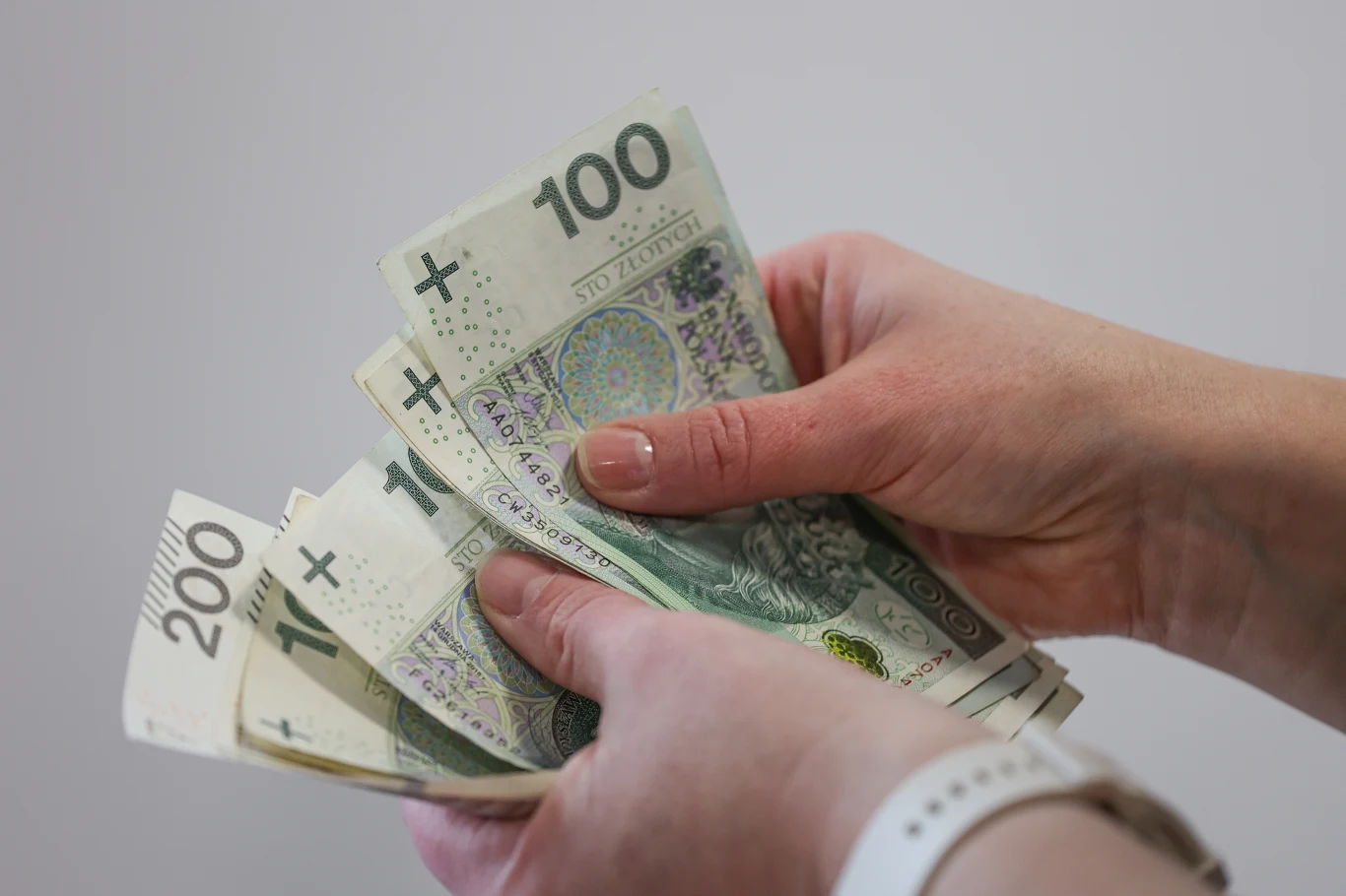 Dodatek za wysługę lat. Komu należą się te pieniądze? Dłoń trzymająca rozłożone banknoty 100 i 200 złotych, odnosząca się do dodatku za wysługę lat.