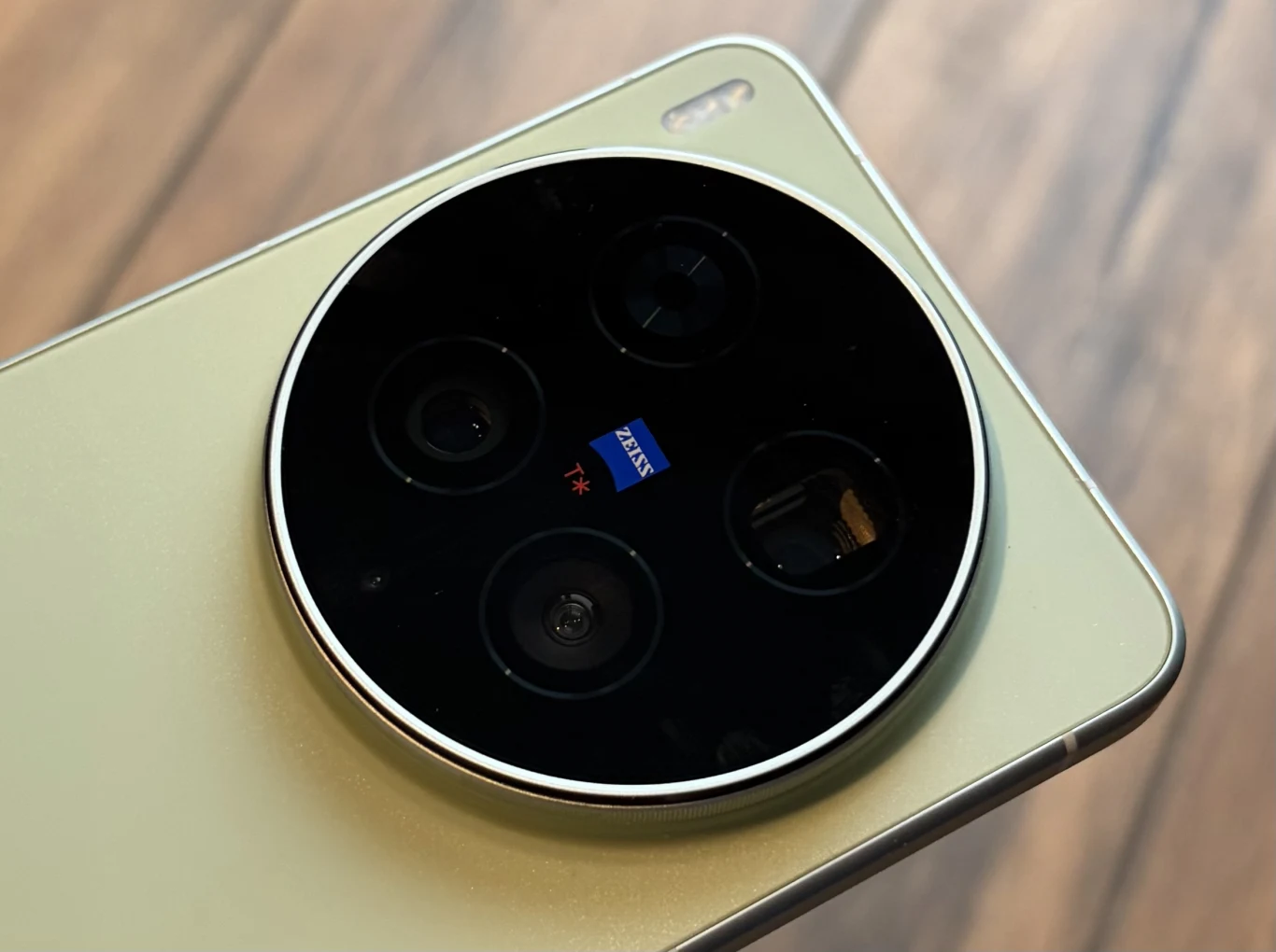 okrągły moduł aparatu z czterema obiektywami i logo Zeiss na złotym tle smartfona