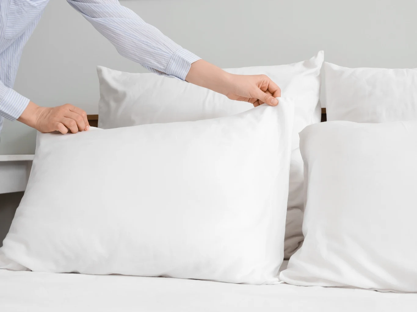 Osoba układa czystą, białą poduszkę na łóżku obok innych, równomiernie ułożonych białych poduszek.