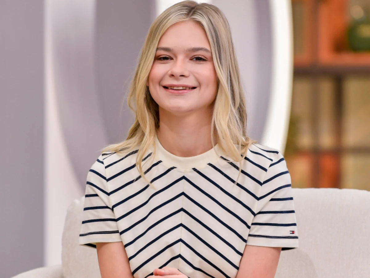 Julia Wróblewska Julia Wróblewska siedzi na jasnej kanapie, ma blond włosy i bluzkę w czarne paski w kształcie litery V.