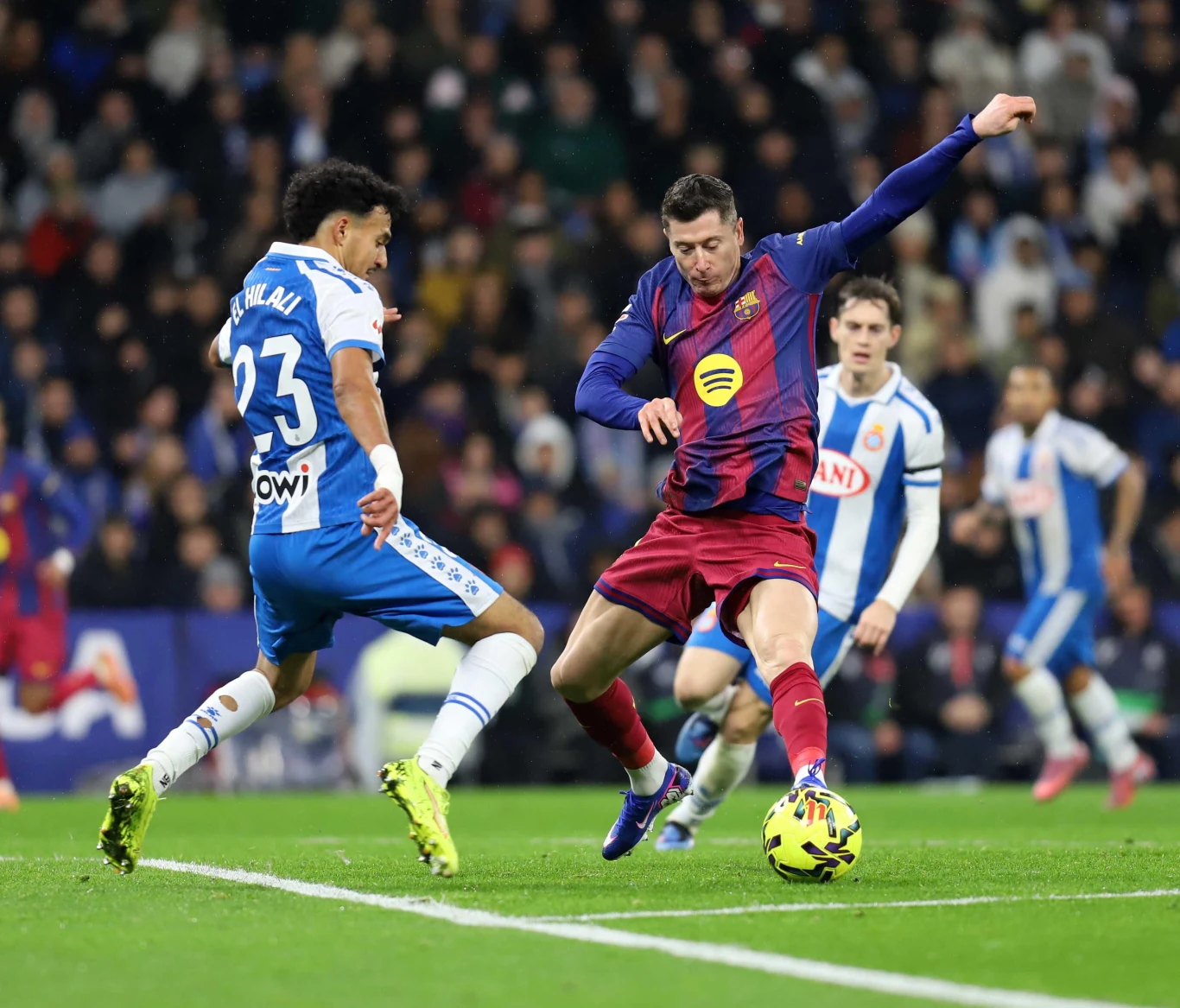 Robert Lewandowski w meczu Espanyol - FC Barcelona Robert Lewandowski w barwach Barcelony kopie piłkę, zawodnik Espanyolu próbuje go zablokować podczas meczu.