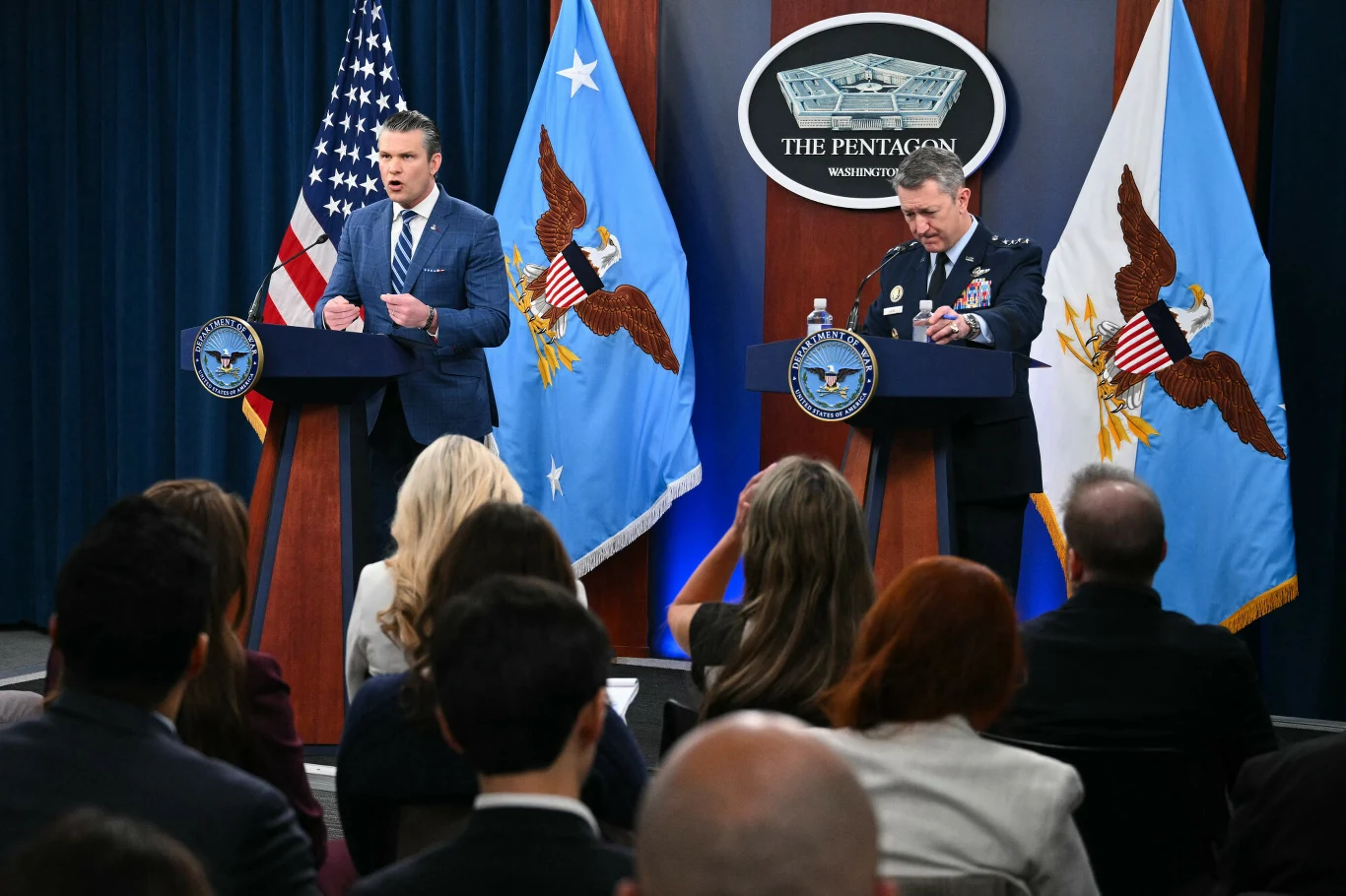 Konferencja sekretarza wojny USA Hegsetha i szefa połączonych sztabów gen. Caine'a Sekretarz wojny USA Pete Hegseth i generał Dan Caine stoją za podium podczas konferencji prasowej w Pentagonie, na tle flag USA i Departamentu Obrony.