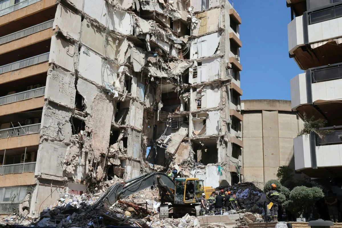 zawalony budynek mieszkalny z dużymi zniszczeniami, gruzy oraz uszkodzone ściany, ratownicy i ekipa ratunkowa pracujący przy zawalonej konstrukcji, widoczny ciężki sprzęt służący do wydobywania osób lub usuwania gruzu