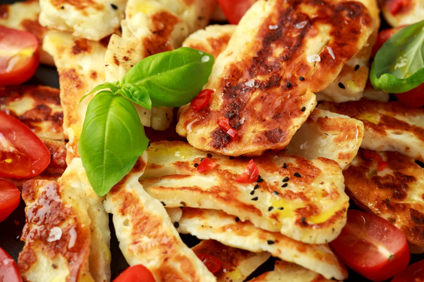 Halloumi świetnie smakuje zarówno smażony jak i pieczony - wyjątkowy smak sera można podbić przyprawami plastry grillowanego sera halloumi posypane przyprawami, udekorowane świeżą bazylią i kawałkami czerwonych pomidorów koktajlowych