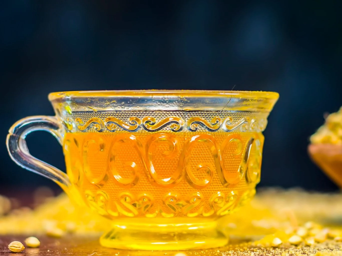 Woda jeera to napój pochodzący z ajurwedy. Wspiera trawienie i odchudzanie Filiżanka z wodą jeera na drewnianym tle, otoczona ziarnami kminu rzymskiego, jasnożółty napój.