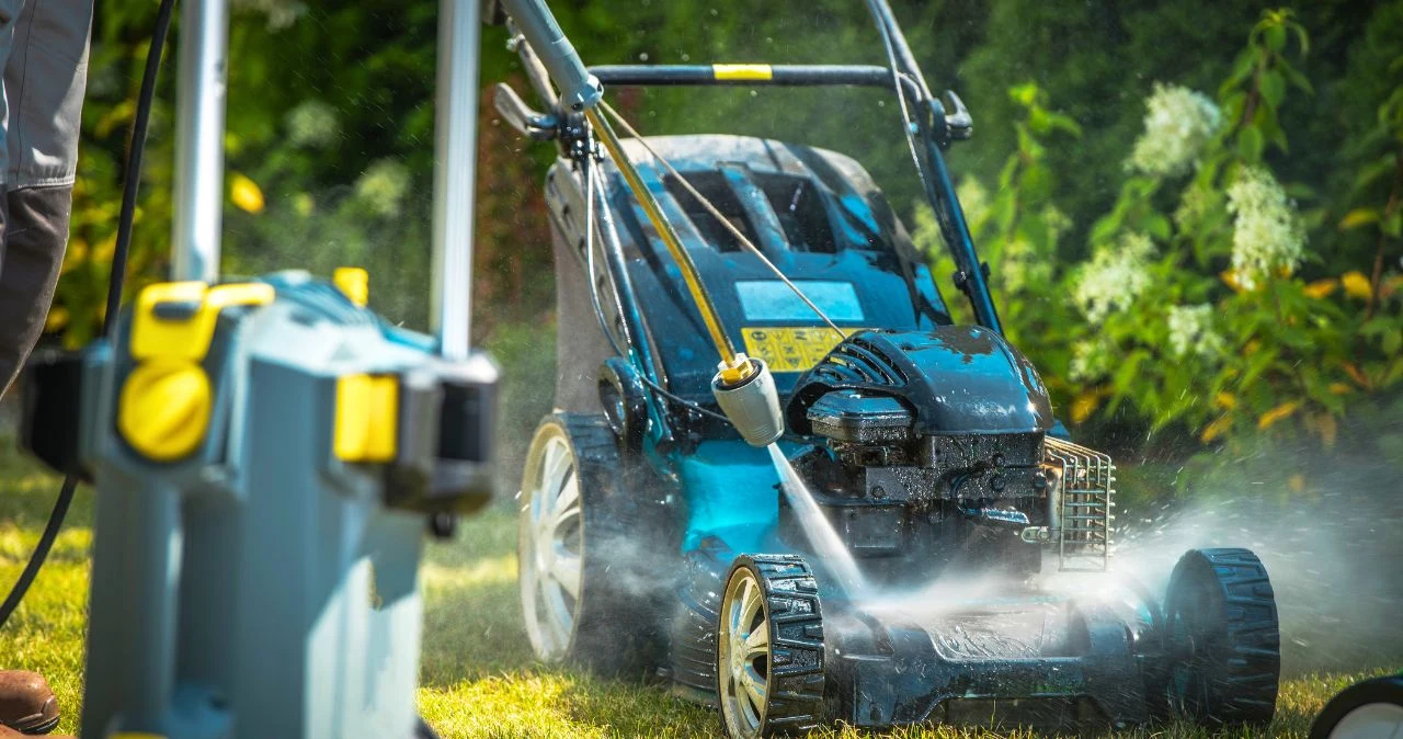 Masz ogród lub działkę? Ten sprzęt z Biedronki będzie hitem od poniedziałku - klienci już czekają Mycie kosiarki ogrodowej myjką ciśnieniową, silny strumień wody, w tle rośliny ogrodowe