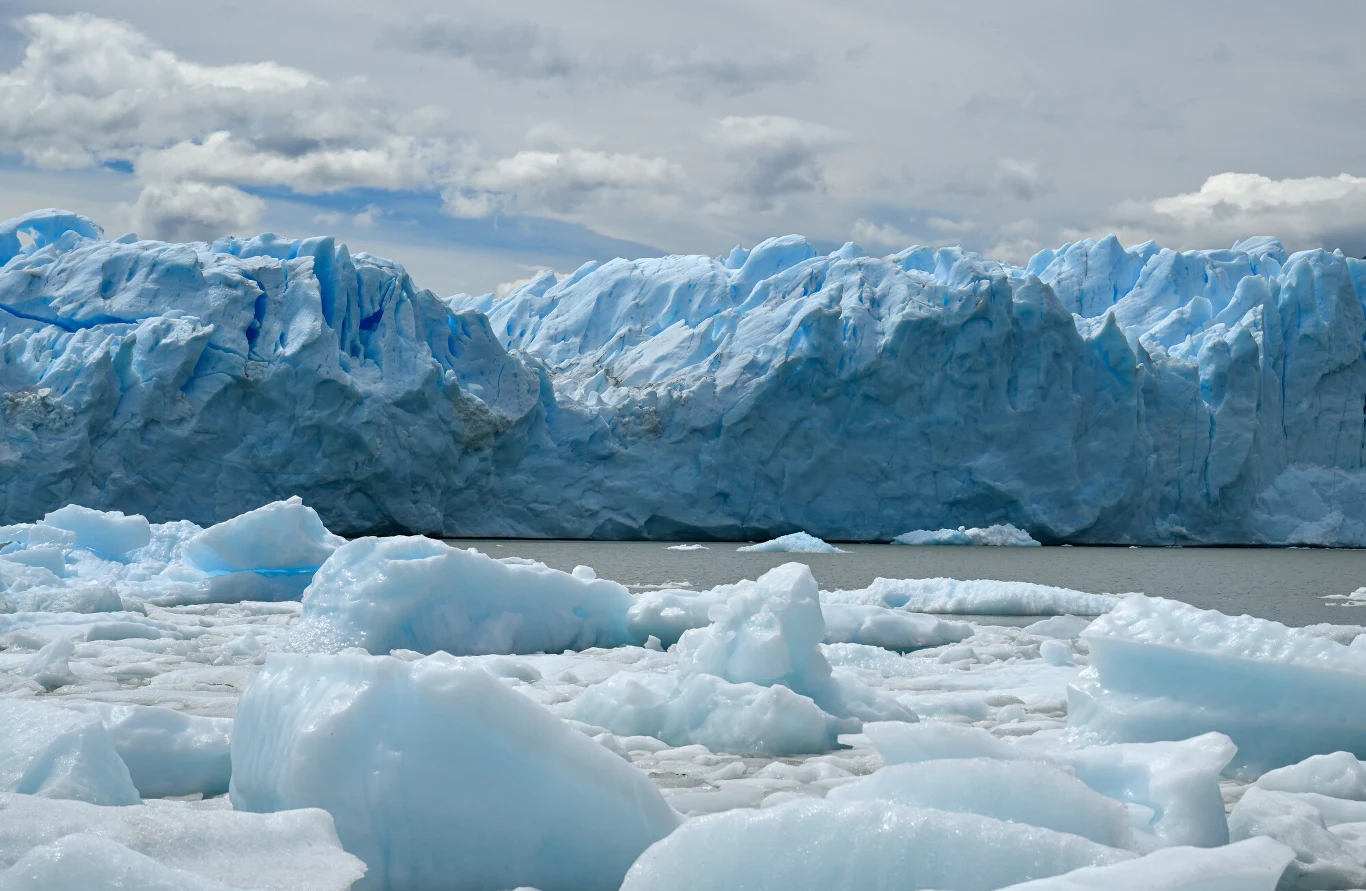 30 km długości lodowca Perito Moreno Błękitny lodowiec z ostrymi krawędziami rozciąga się w tle, a na pierwszym planie unosi się na wodzie wiele sporych, połyskujących kawałków lodu.
