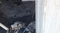 spalone drewniane belki leżą na ziemi przed wejściem do nadpalonego budynku, w podłożu widoczny wykop z metalowymi elementami i niebieską rurą
