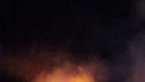 intensywny pożar obejmuje dach budynku nocą, płomienie wydobywają się z górnej części konstrukcji, wokół unosi się gęsty dym
