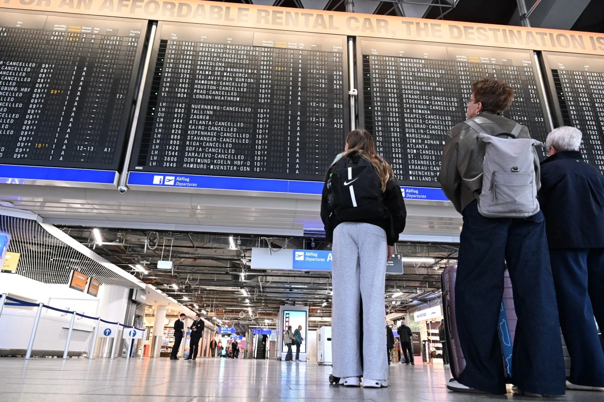 Pasażerowie na lotnisku we Frankfurcie (tam akurat odwołano loty z powodu strajków) trzy osoby stoją pod dużą tablicą odlotów na lotnisku, skupiając wzrok na informacjach o lotach wyświetlanych na ekranach
