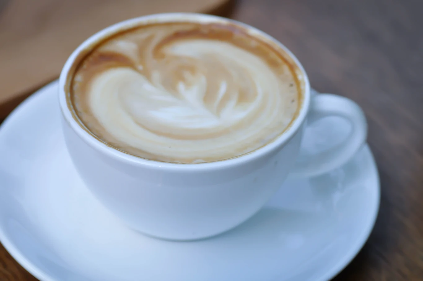 Wprowadź jedną zmianę podczas przyrządzania kawy Biała filiżanka cappuccino z kremową pianką i mlecznym wzorem na powierzchni, na białym spodku.