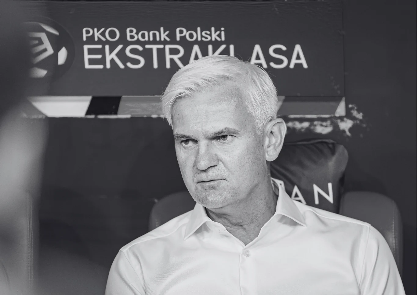 Jacek Magiera zmarł w wieku 49 lat starszy mężczyzna o siwych włosach w białej koszuli siedzi na tle logo PKO Bank Polski Ekstraklasa, patrząc poważnie w kierunku rozmówcy