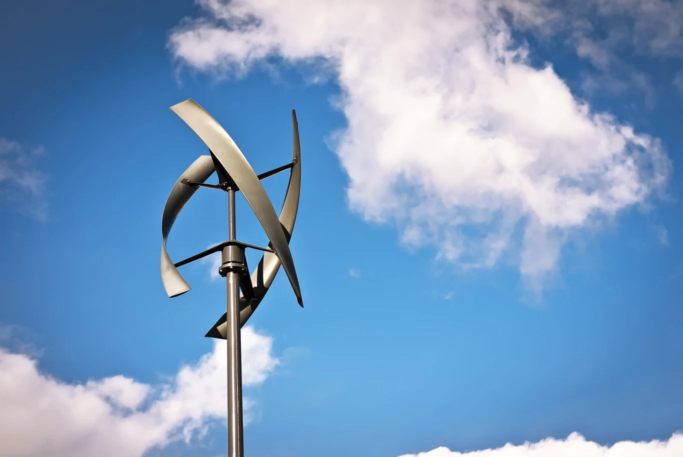 pionowa turbina wiatrowa o nowoczesnym designie na tle niebieskiego nieba z białymi chmurami