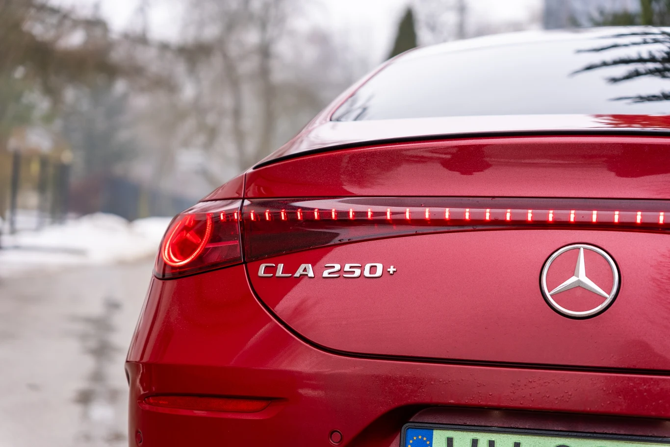 czerwony Mercedes CLA 250+ z widocznym podświetlanym pasem tylnych świateł LED oraz chromowanym logo marki na klapie bagażnika