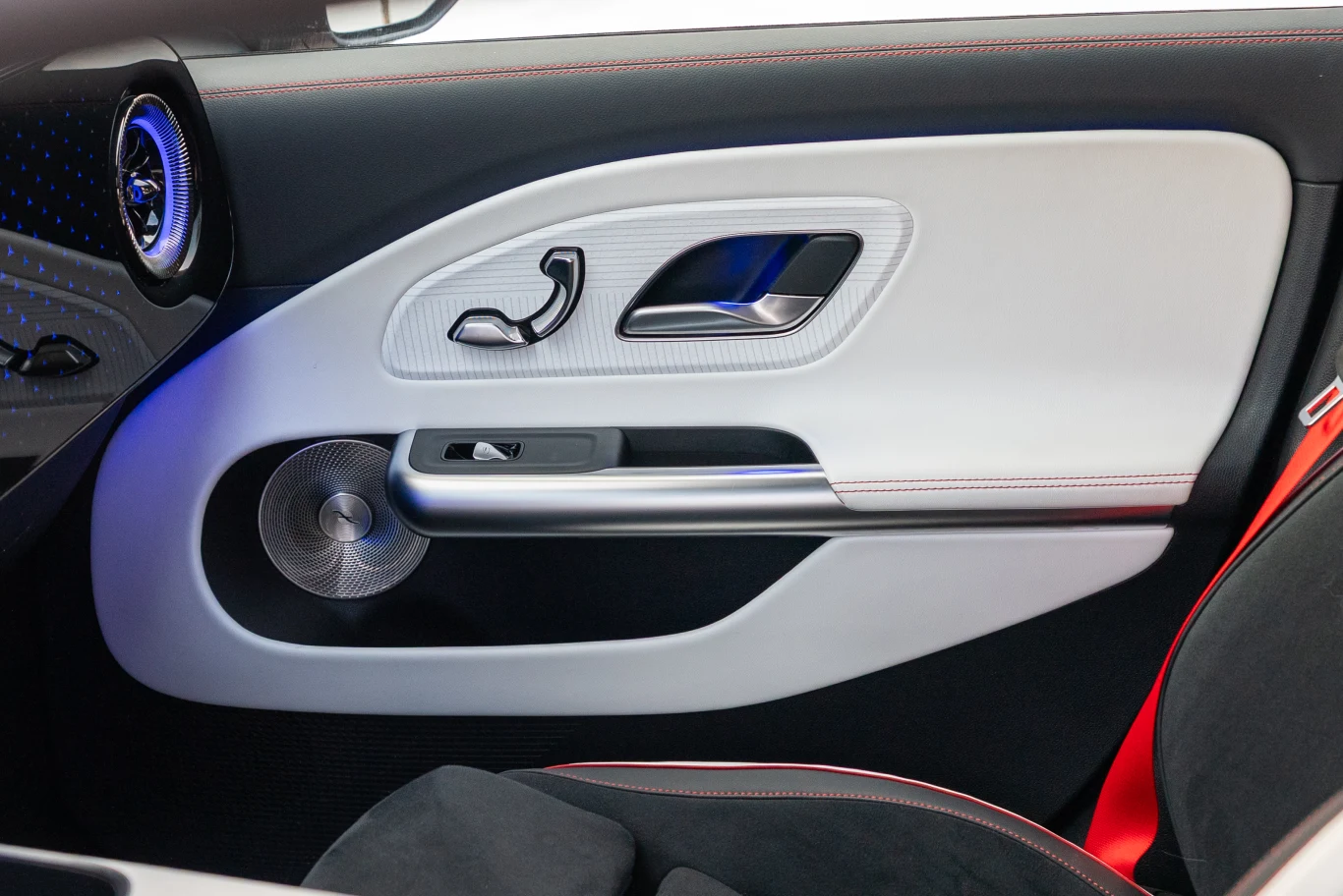 nowoczesny panel drzwiowy samochodu z jasnym wykończeniem, srebrną klamką, przyciskiem elektrycznym do obsługi szyb oraz okrągłym głośnikiem audio umieszczonym w dolnej części