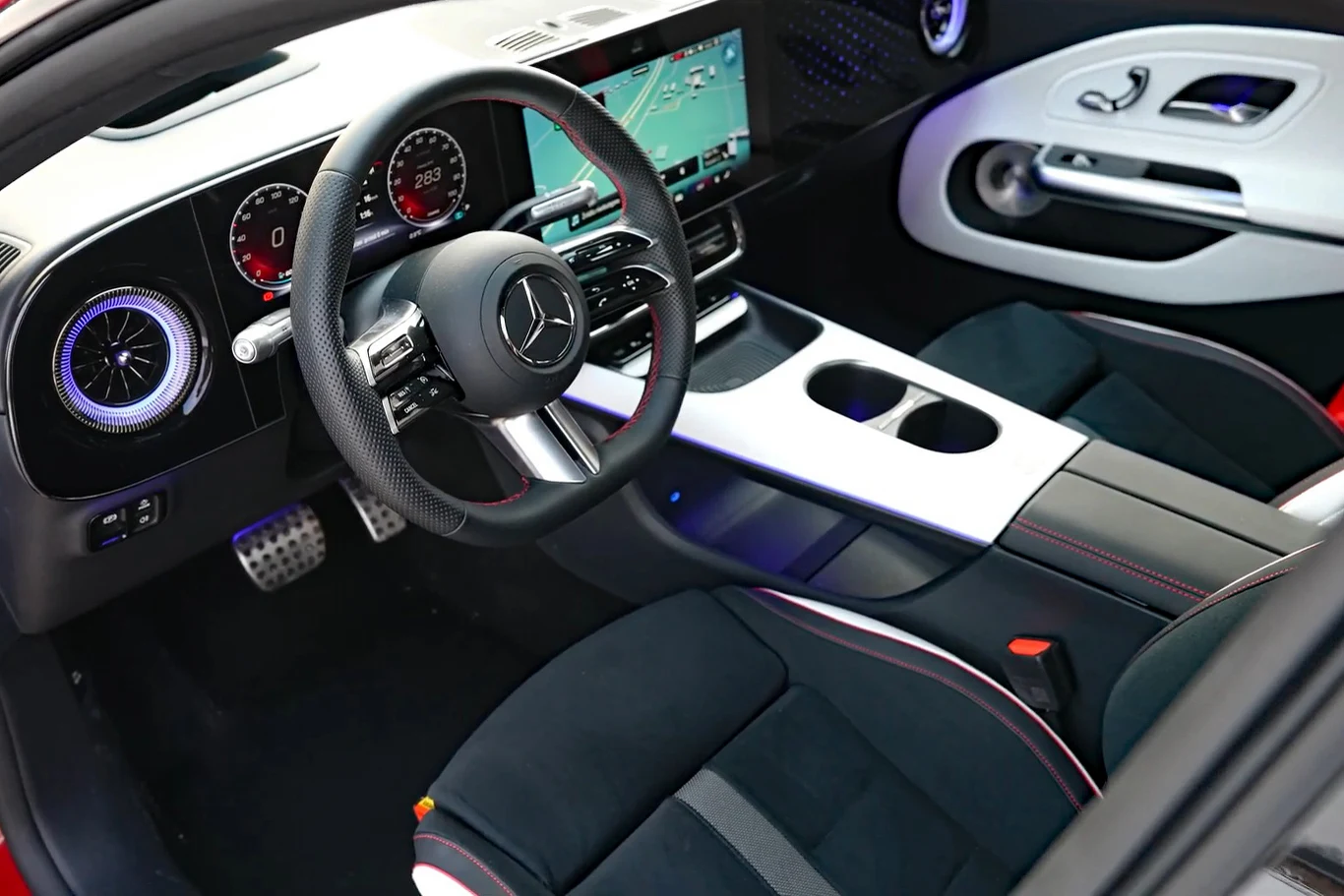 luksusowe wnętrze samochodu marki Mercedes z nowoczesną deską rozdzielczą, cyfrowymi zegarami, dużym ekranem multimedialnym oraz sportową kierownicą wykończoną skórą