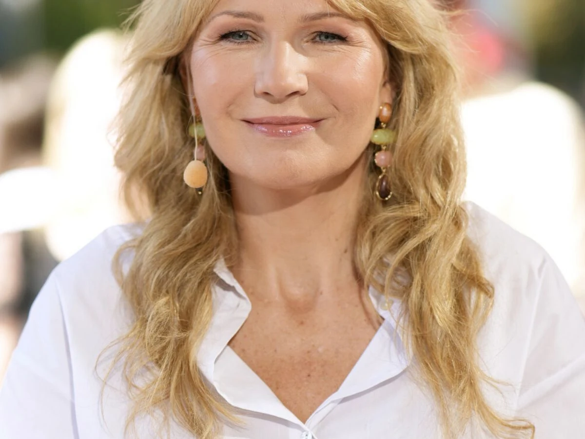 Anna Guzik Anna Guzik w białej koszuli, z długimi blond falowanymi włosami, delikatnym makijażem i kolorowymi kolczykami.