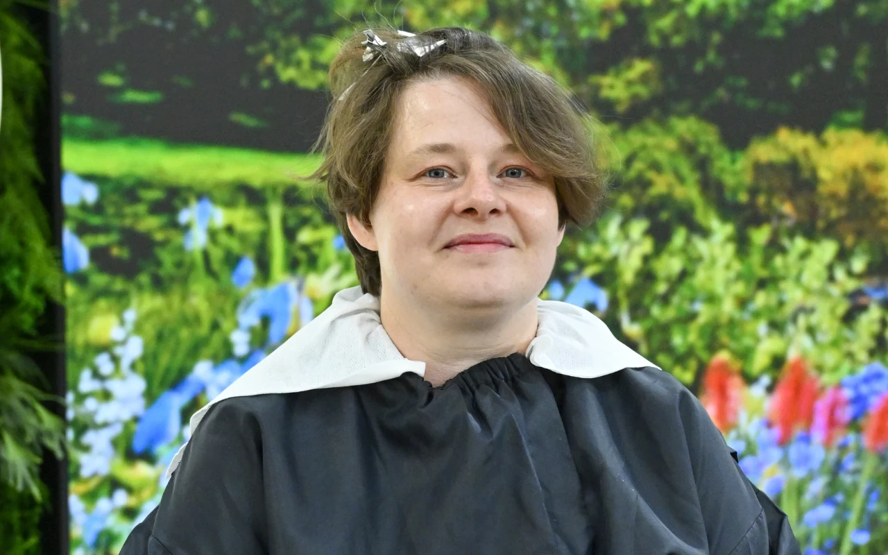 Metamorfoza Małgorzaty zaczęła się od zmiany koloru włosów kobieta z krótkimi, brązowymi włosami i delikatnym uśmiechem na twarzy, ubrana w pelerynę fryzjerską, na włosach znajdują się srebrne klamerki, w tle kolorowe kwiaty i zielona roślinność