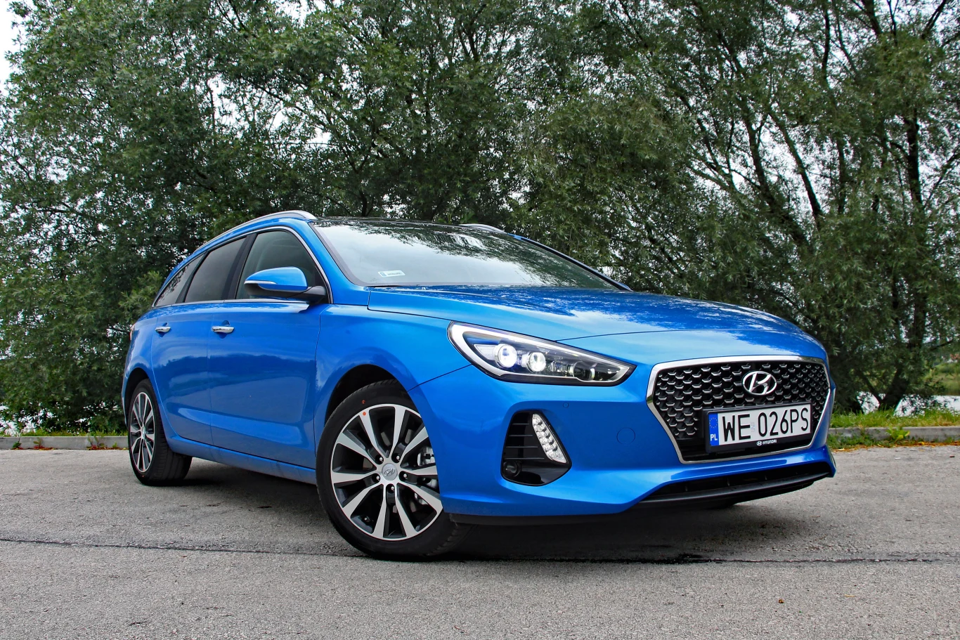 Hyundai i30 kombi Hyundai i30 kombi w kolorze niebieskim z nowoczesnym grillem, zaparkowany na asfalcie, w tle zielone drzewa