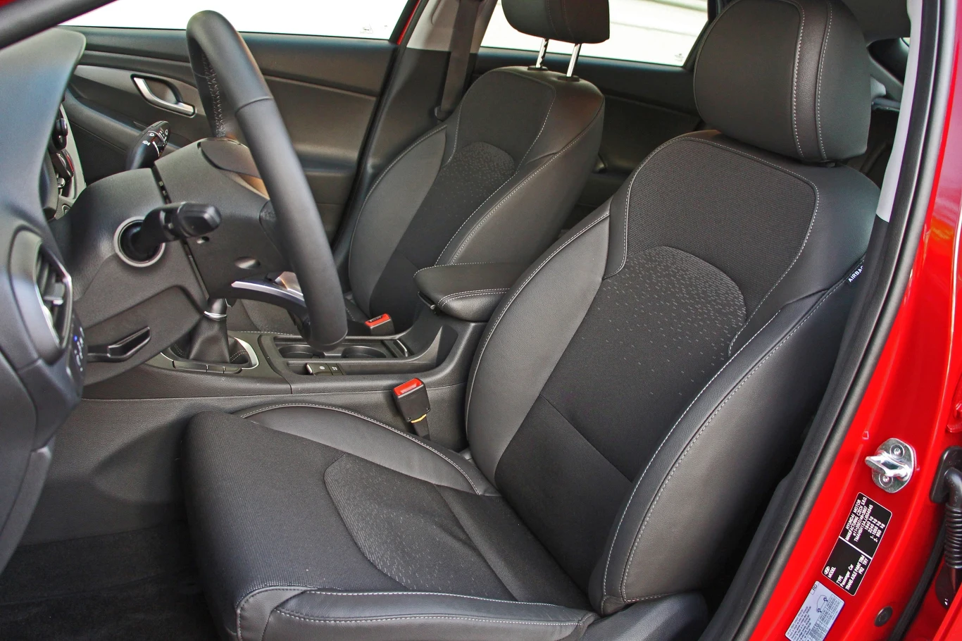 Hyundai i30 czarne, tapicerowane fotele samochodowe z wyraźnymi przeszyciami oraz konsola środkowa wyposażona w manualną skrzynię biegów i dźwignię hamulca ręcznego, wnętrze utrzymane w nowoczesnym stylu