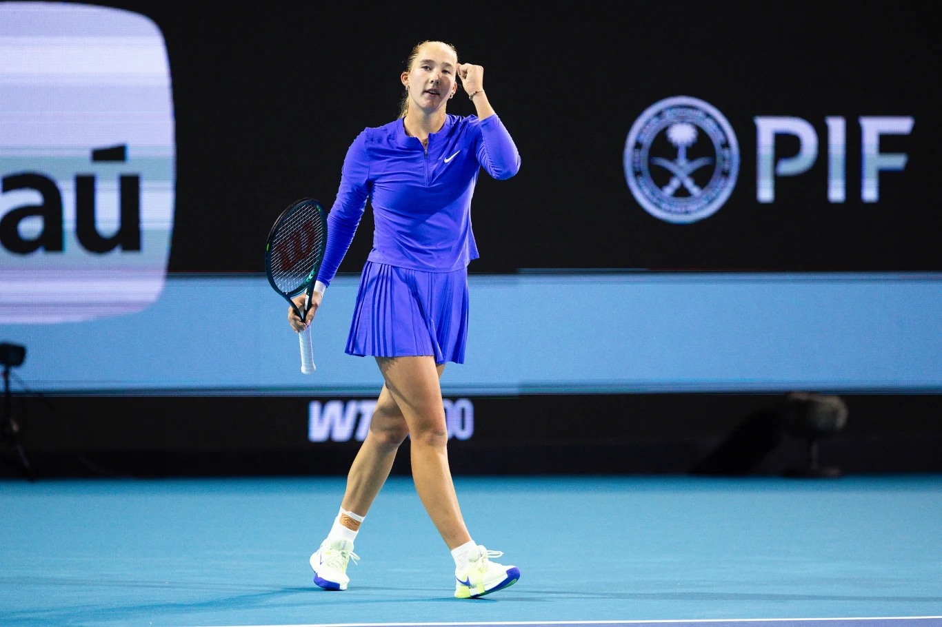 Mirra Andriejewa tenisistka ubrana w niebieski strój sportowy z wyrazem triumfu na twarzy, zaciśniętą pięścią i rakietą w lewej ręce podczas meczu na korcie