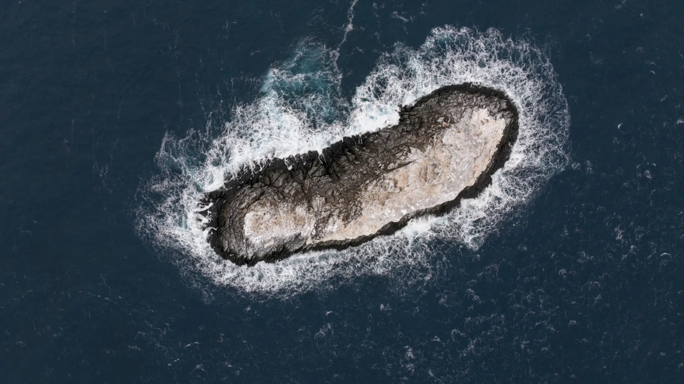 Wyspa była wcześniej błędnie oznaczona na mapach. Samotna, skalista wyspa o nieregularnym kształcie otoczona wzburzonymi falami oceanu, kontrastująca ciemnym kolorem skał z głęboką barwą wody.