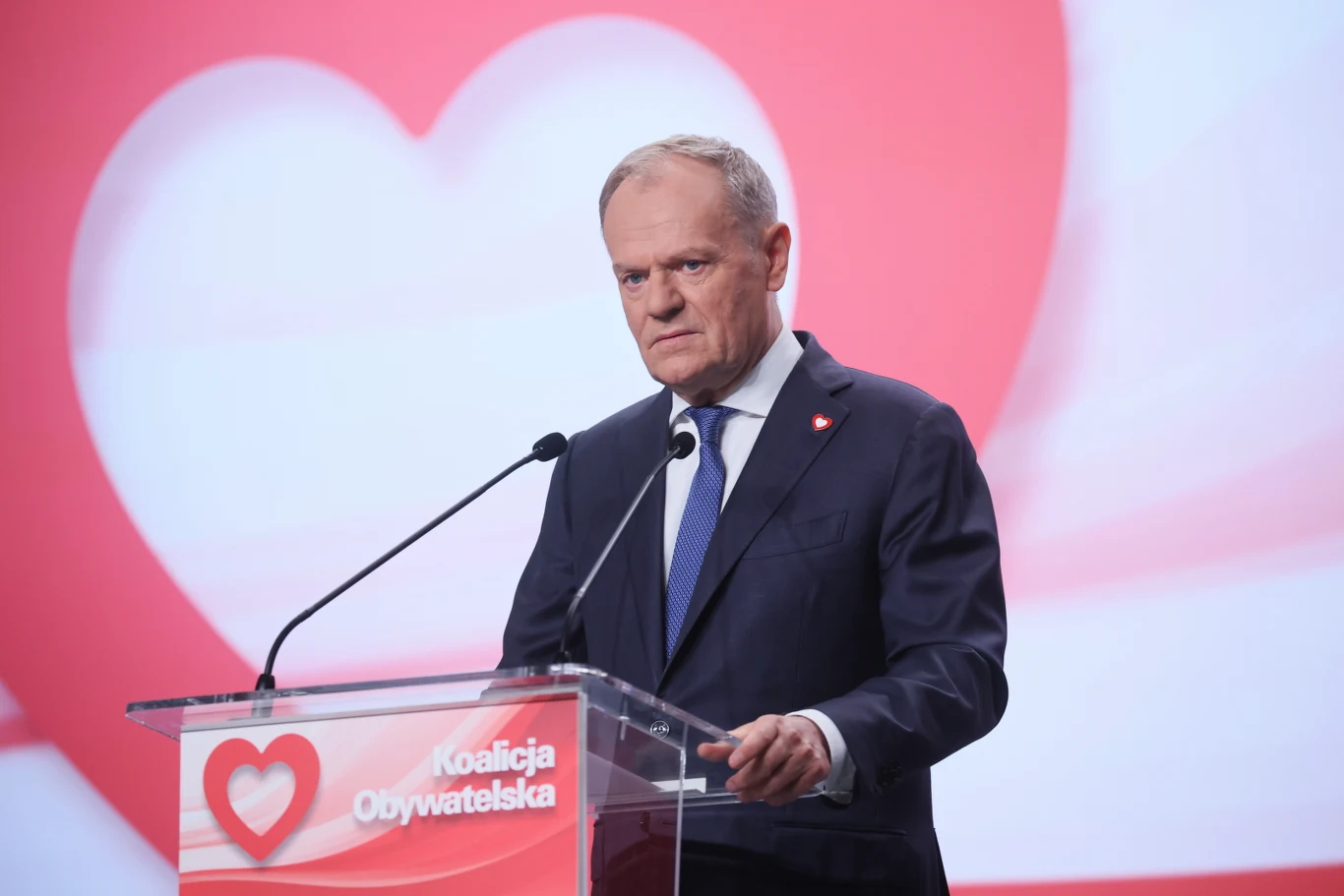 Premier Donald Tusk podczas Rady Krajowej Koalicji Obywatelskiej Donald Tusk przy mównicy z logo Koalicji Obywatelskiej na tle dużego czerwonego serca.