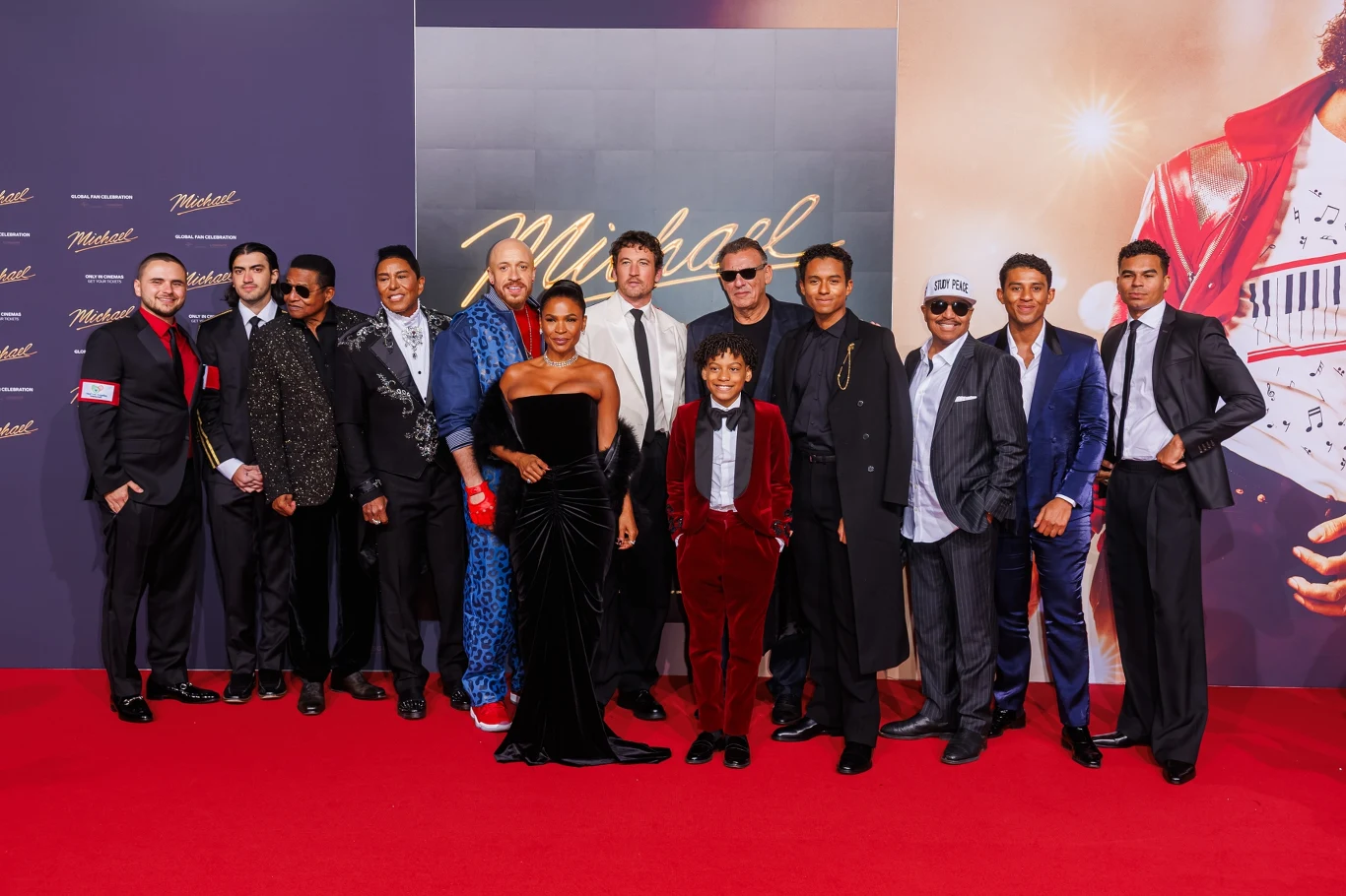 Premiera filmu "Michael" w Berlinie Grupa elegancko ubranych osób pozuje na czerwonym dywanie na tle scenografii związanej z musicalem 'Michael', większość mężczyzn ma na sobie garnitury, a jedna kobieta suknię wieczorową, całość utrzymana w atmosferze prestiżowego wydarzenia branżowego.