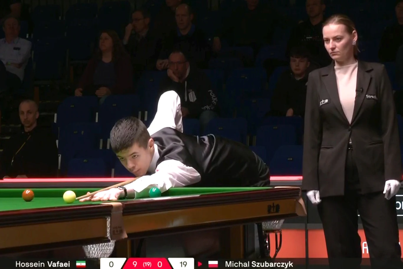 Michał Szubarczyk w meczu z Hosseinem Vafaeim snookerzysta w czarnym kamizelce wykonuje precyzyjny strzał do bili przy stole do snookera, obok stoi sędzina uważnie obserwująca grę