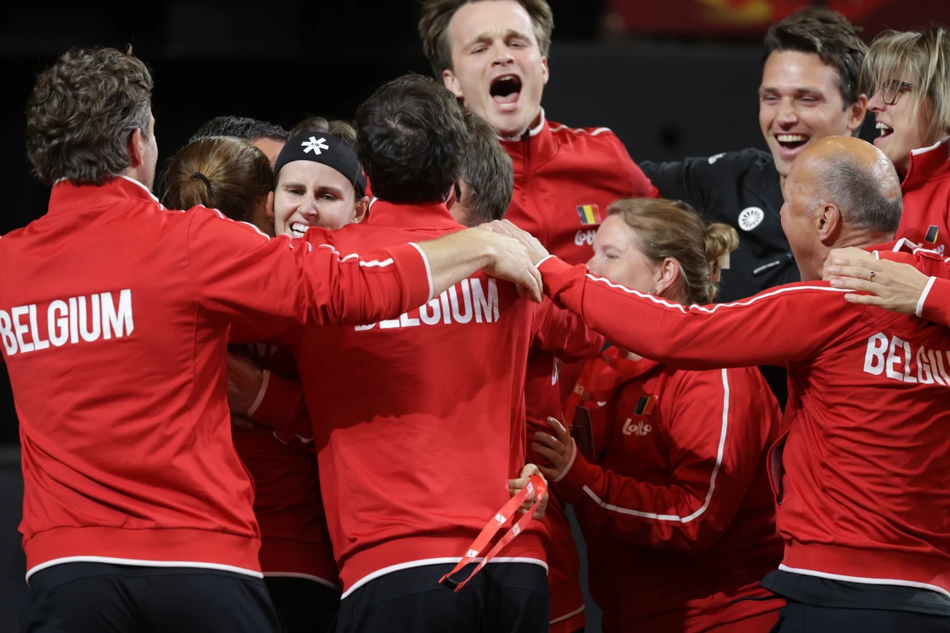 Radość reprezentacji Belgii po sensacyjnym awansie grupa sportowców ubranych w czerwone dresy z napisem 'Belgium' świętuje razem, obejmując się i wyrażając radość po wspólnym sukcesie