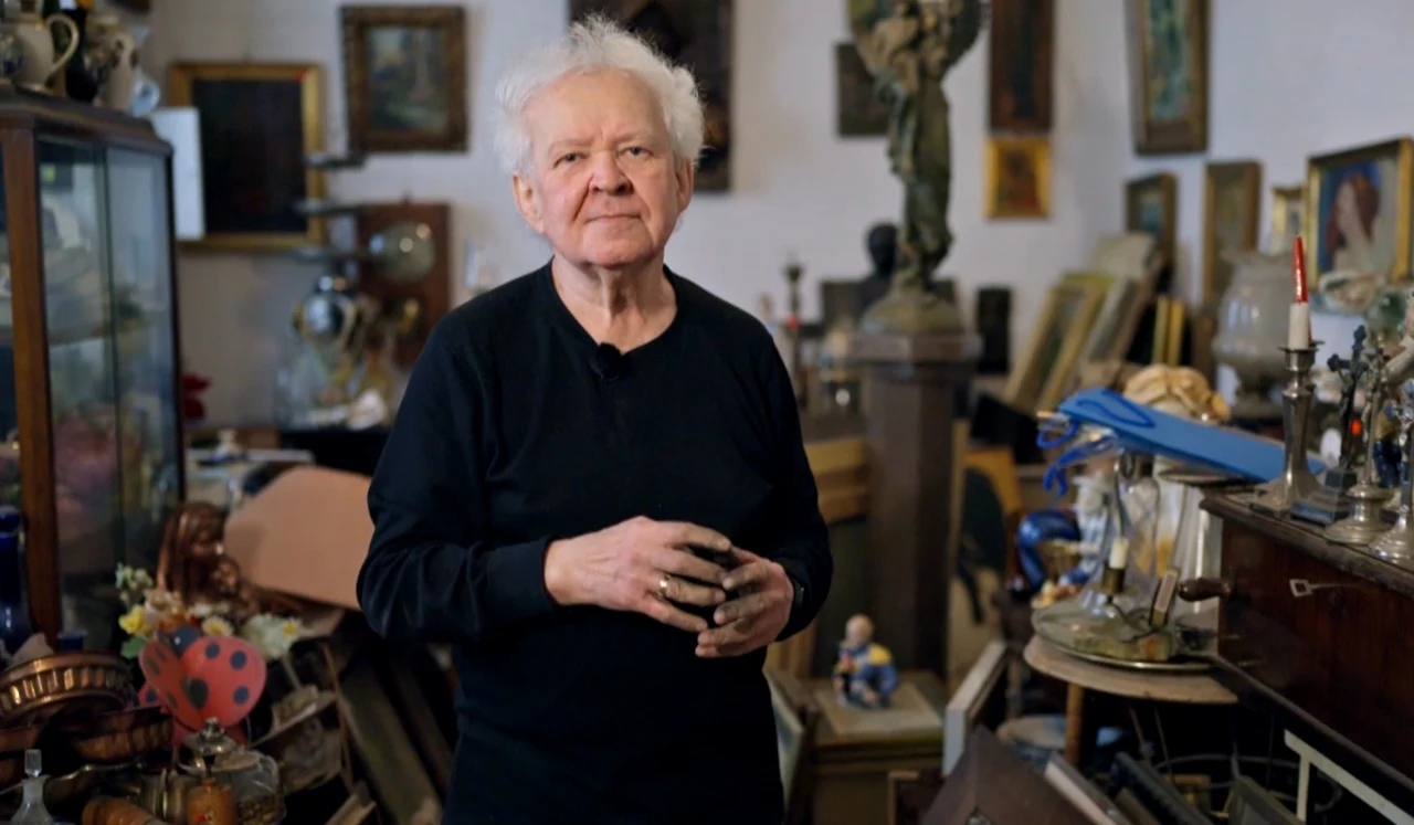 Jan Kaliński w swym "królestwie" Starszy mężczyzna o siwych włosach w czarnym swetrze stoi wśród licznych antyków i dzieł sztuki, otoczony obrazami, figurkami oraz różnorodnymi bibelotami w klimatycznym, zagraconym wnętrzu.