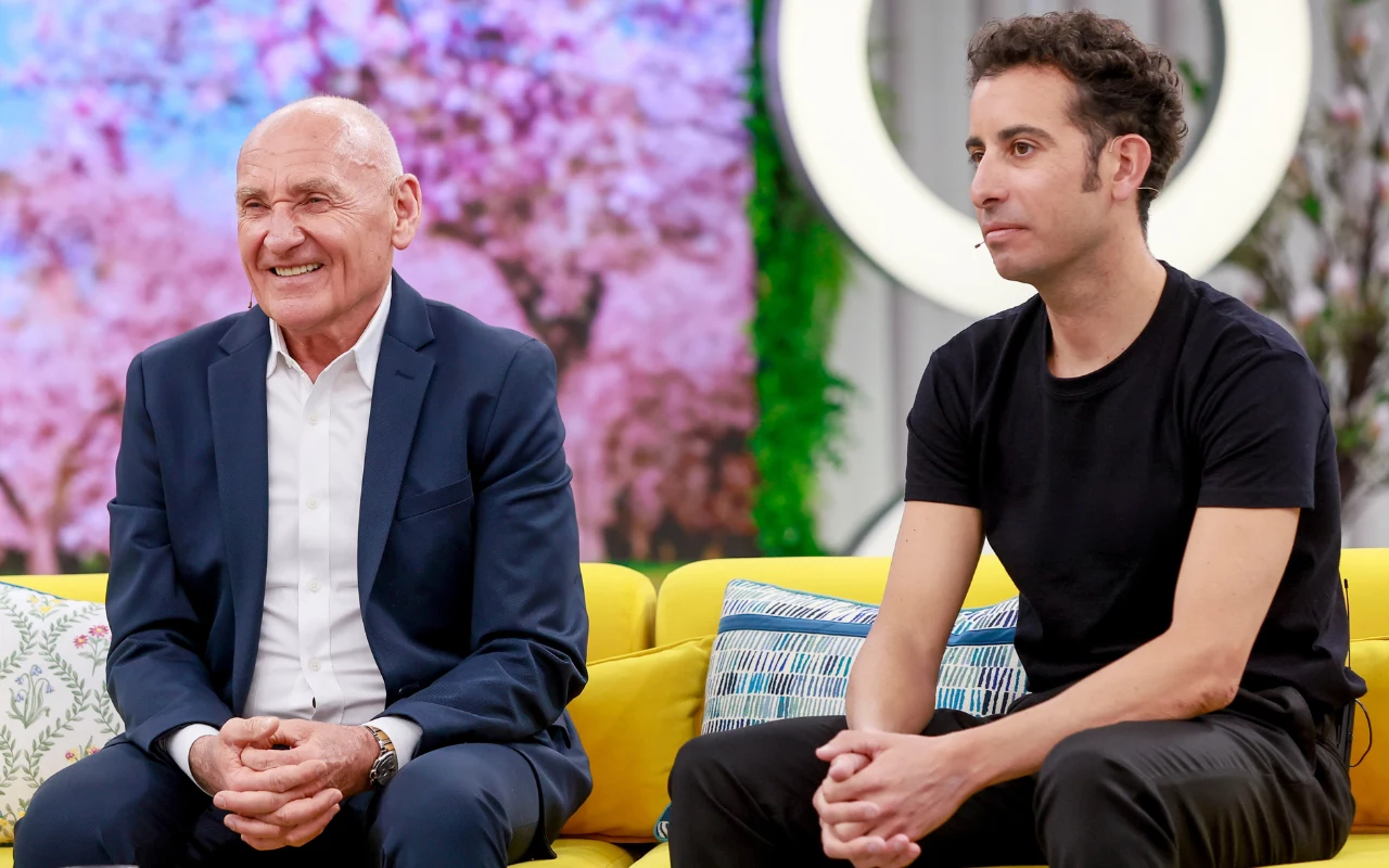 Czesław Lang i Fabio Aru w "halo tu polsat" Dwóch mężczyzn siedzi na żółtej sofie; starszy w eleganckim garniturze uśmiecha się szeroko, młodszy ubrany na czarno patrzy poważnie w bok; w tle kolorowa, rozmyta dekoracja przypominająca kwitnące drzewa.