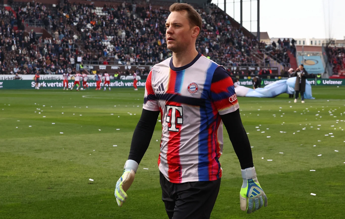piłkarz w stroju bramkarskim Bayernu Monachium z rękawicami bramkarskimi idzie po murawie stadionu przy dużej liczbie kibiców na trybunach