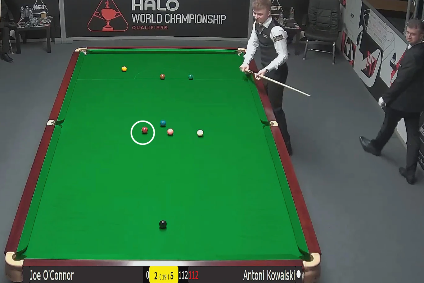 Stół bilardowy z rozłożonymi bilami, dwóch zawodników w eleganckich kamizelkach podczas rozgrywki snookera, wyświetlony wynik meczu oraz logo turnieju HALO World Championship na ścianie w tle.