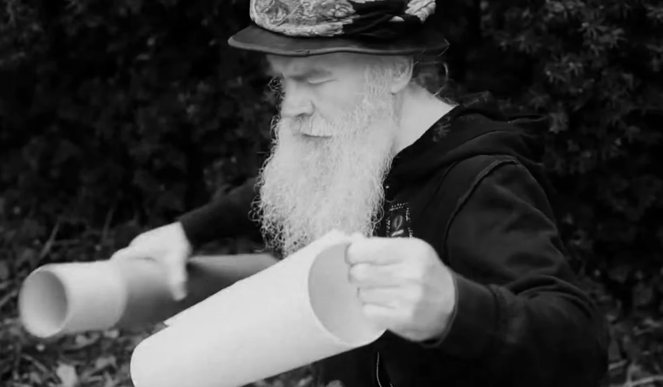 Krzysztof "Pinki" Brandt w teledysku "Pinki to jest zawodnik" Krzysztof "Pinki" Brandt z długą siwą brodą i w kapeluszu gra na dwóch dużych tubach w plenerze, kadr z teledysku