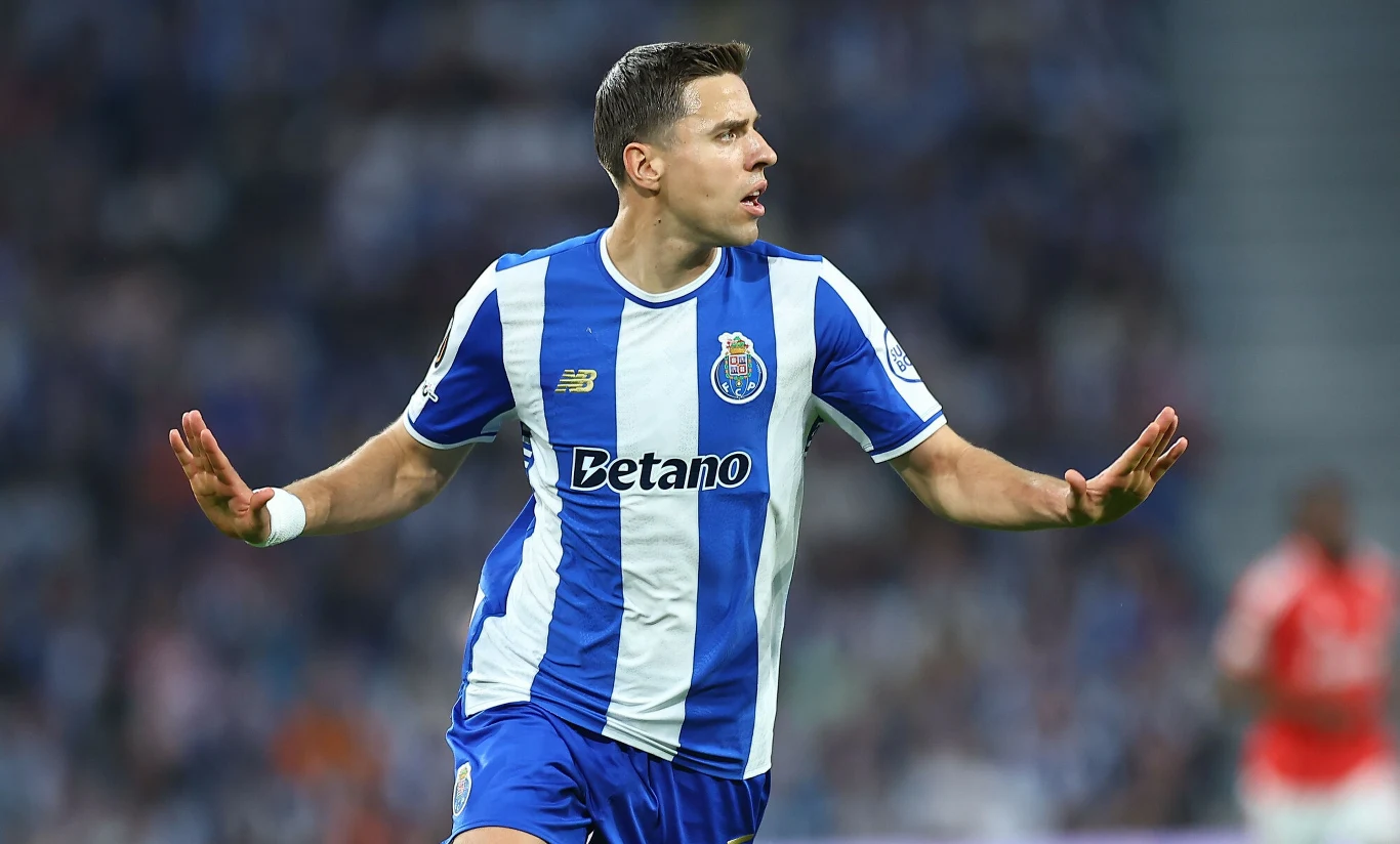 Piłkarz w niebiesko-białym stroju drużyny FC Porto z rozpostartymi ramionami wykonuje gest świętowania na murawie stadionu podczas meczu piłkarskiego.
