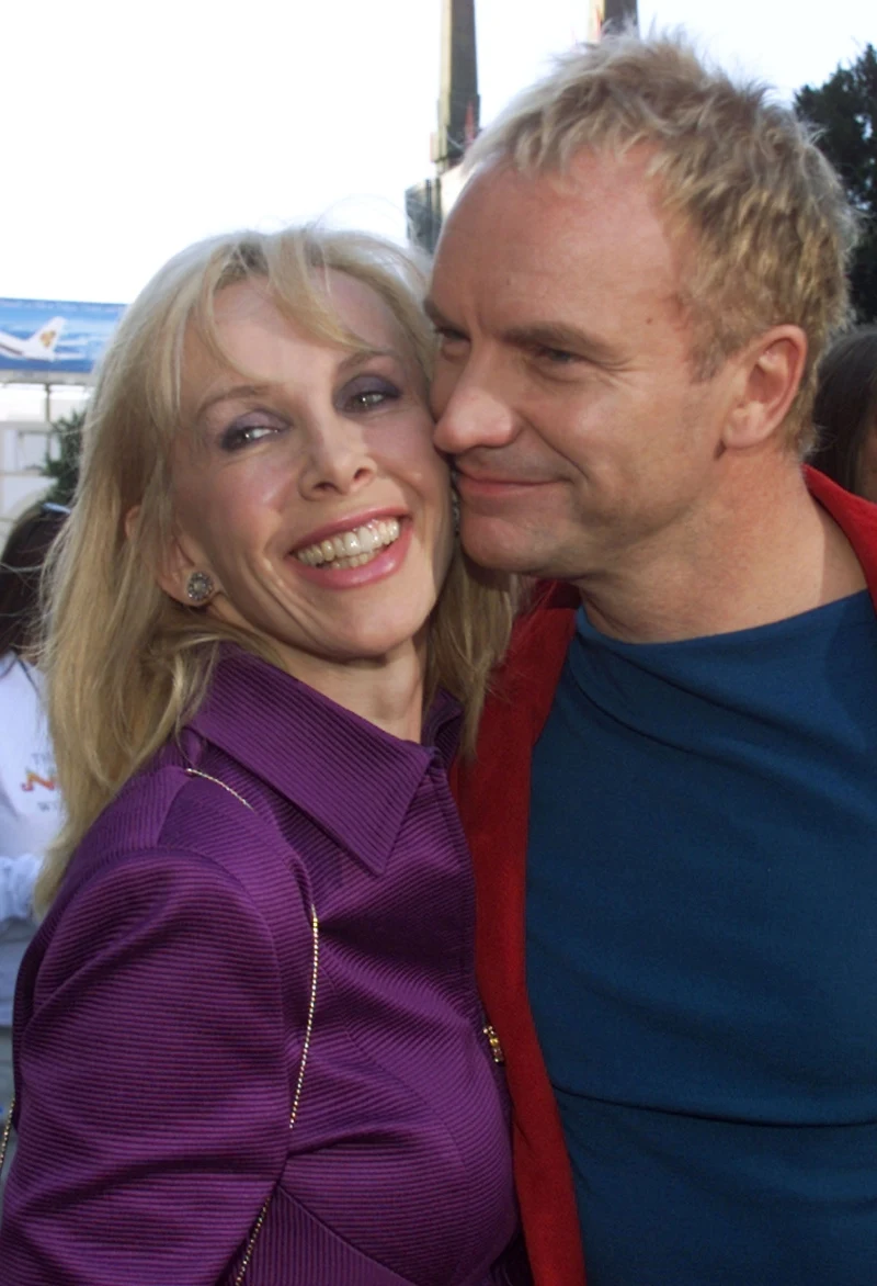 uśmiechnięta kobieta w fioletowej marynarce przytula się do mężczyzny w niebieskiej koszulce i czerwonej kurtce, obydwoje sprawiają wrażenie szczęśliwych i bliskich sobie osób