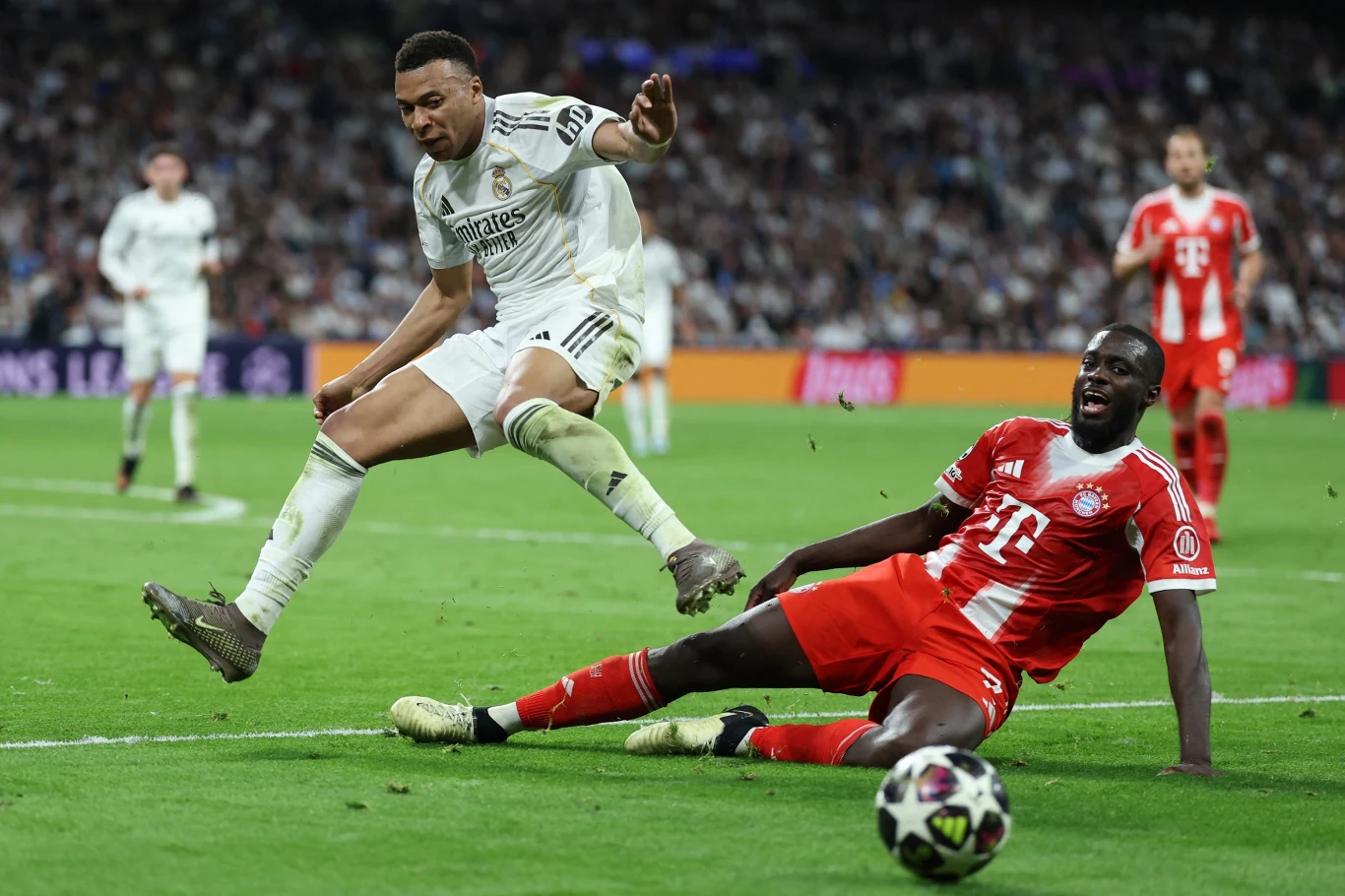 Kylian Mbappe walczy o piłkę z Dayotem Upamecano Kylian Mbappe w białym stroju unika wślizgu Dayota Upamecano w czerwonym podczas meczu na stadionie pełnym kibiców
