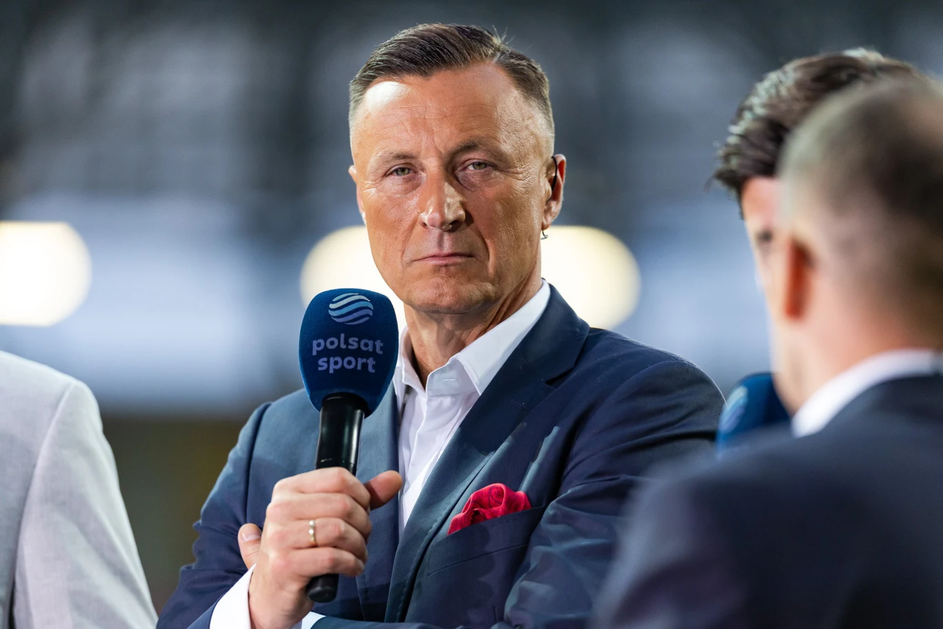 Tomasz Hajto Tomasz Hajto w garniturze z różową poszetką, trzyma mikrofon Polsat Sport podczas relacji sportowej