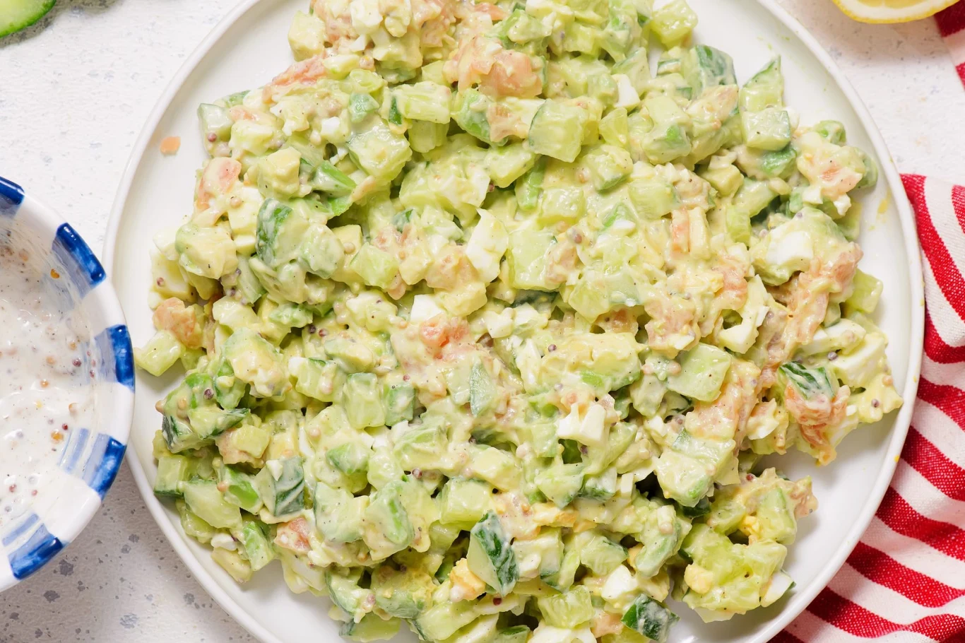 Aksamitna sałatka z łososiem i awokado Sałatka z łososiem, awokado, ogórkiem, koperkiem i jajkiem, podana z jasnym sosem na białym talerzu