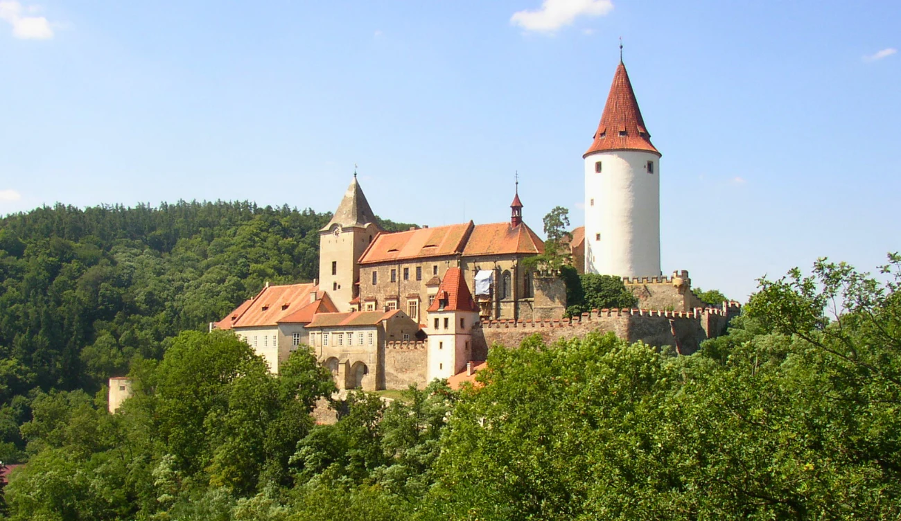 Zamek Křivoklát - czeska perełka z czasów średniowiecza Zamek Křivoklát z białą wieżą i czerwonym dachem, otoczony lasem, widok z góry