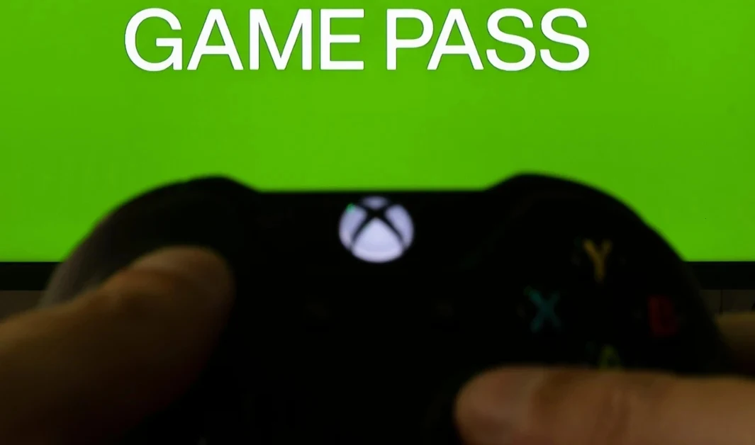Era cyfrowych licencji. Dlaczego twoja kolekcja gier nie istnieje naprawdę? Czarny kontroler Xbox trzymany w dłoniach na tle zielonego ekranu z napisem GAME PASS