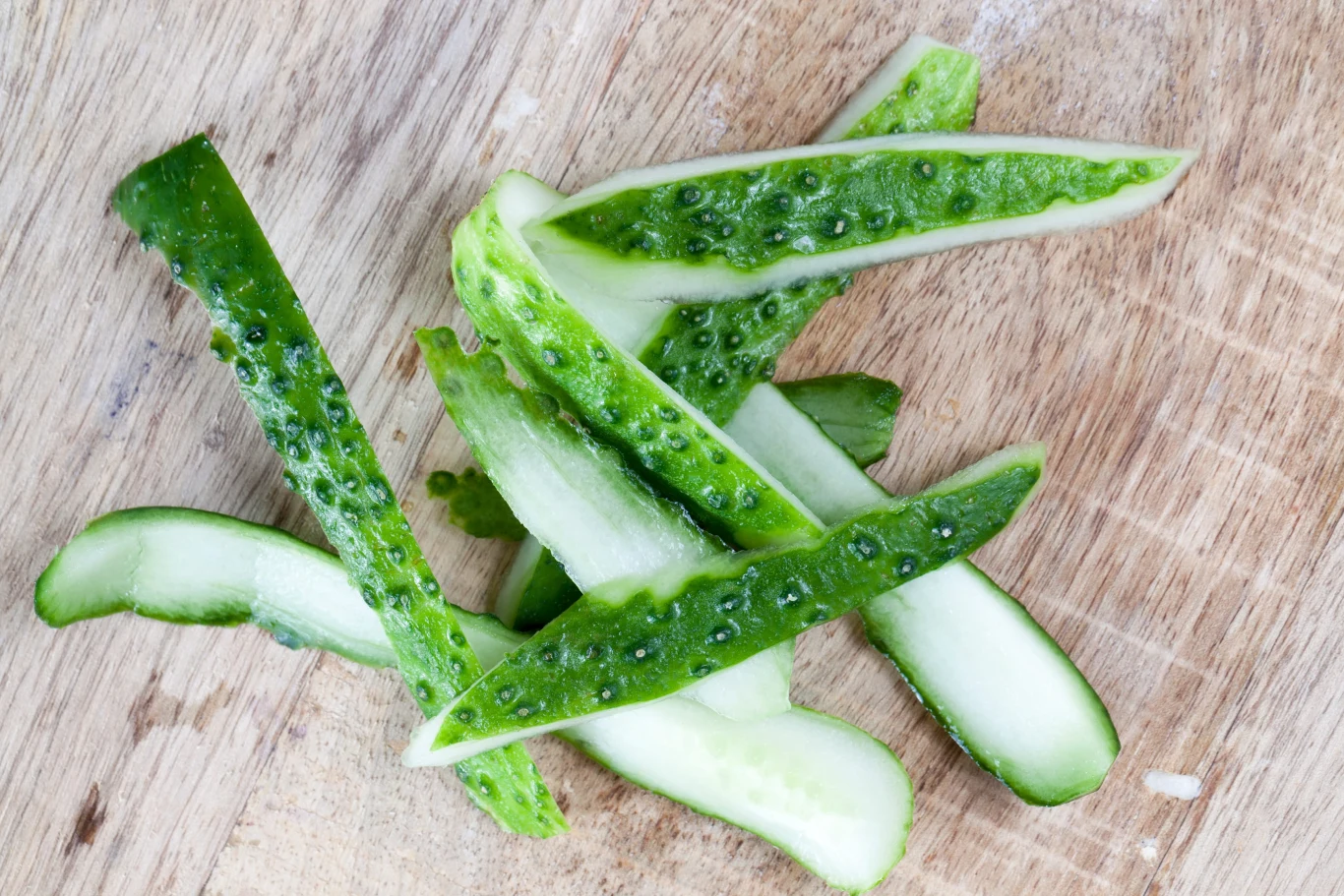Obierki z ogórków można wykorzystać do przygotowania domowej odżywki do roślin doniczkowych i ogrodowych. Sprawdź, jak to zrobić. Zielone obierki ogórka, leżące na drewnianej desce do krojenia.